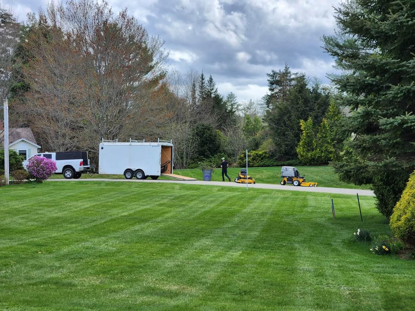 Freshly striped lawn with a landscaping trailer in the driveway